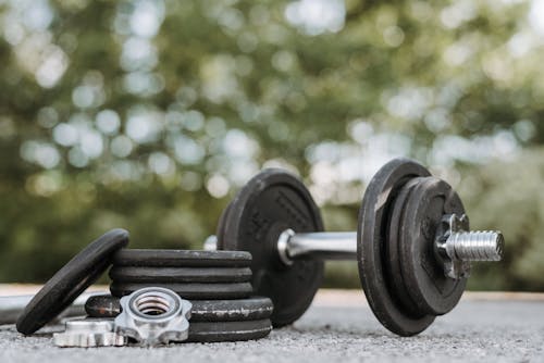 Ground level of adjustable dumbbell on stainless steel bar near plates and screw collars on rough walkway on street