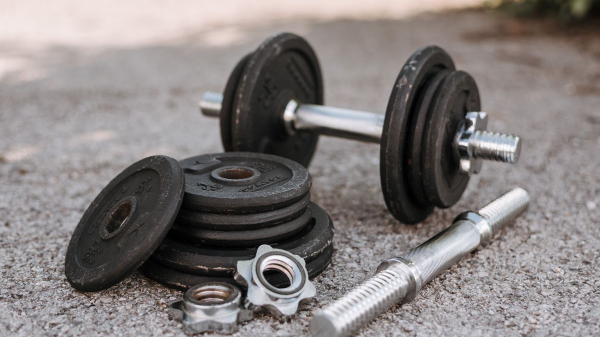 Heavy adjustable dumbbell near cast iron plates and hexagonal collars with stainless steel bar on pavement