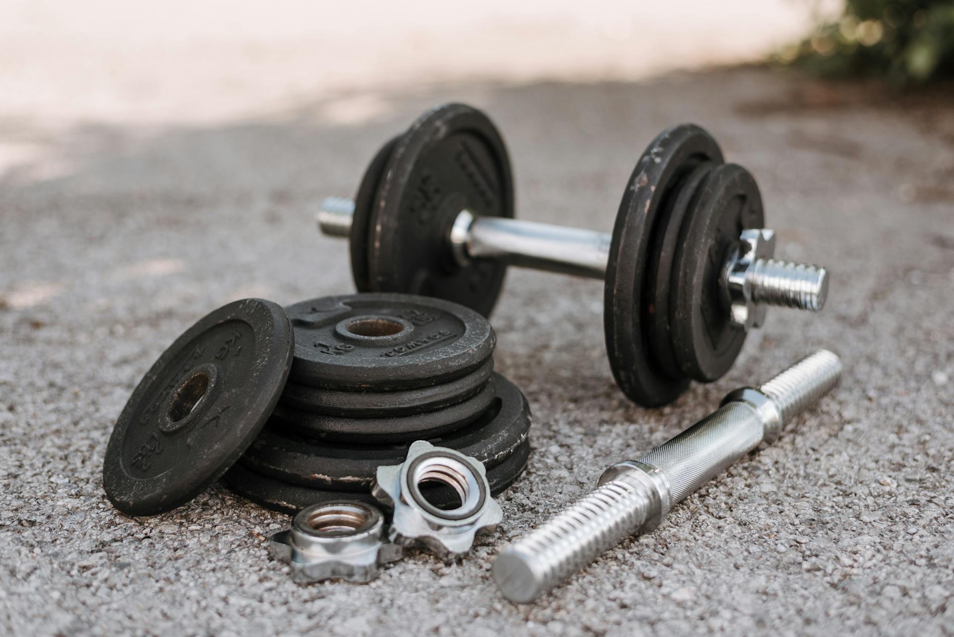 Heavy adjustable dumbbell near cast iron plates and hexagonal collars with stainless steel bar on pavement