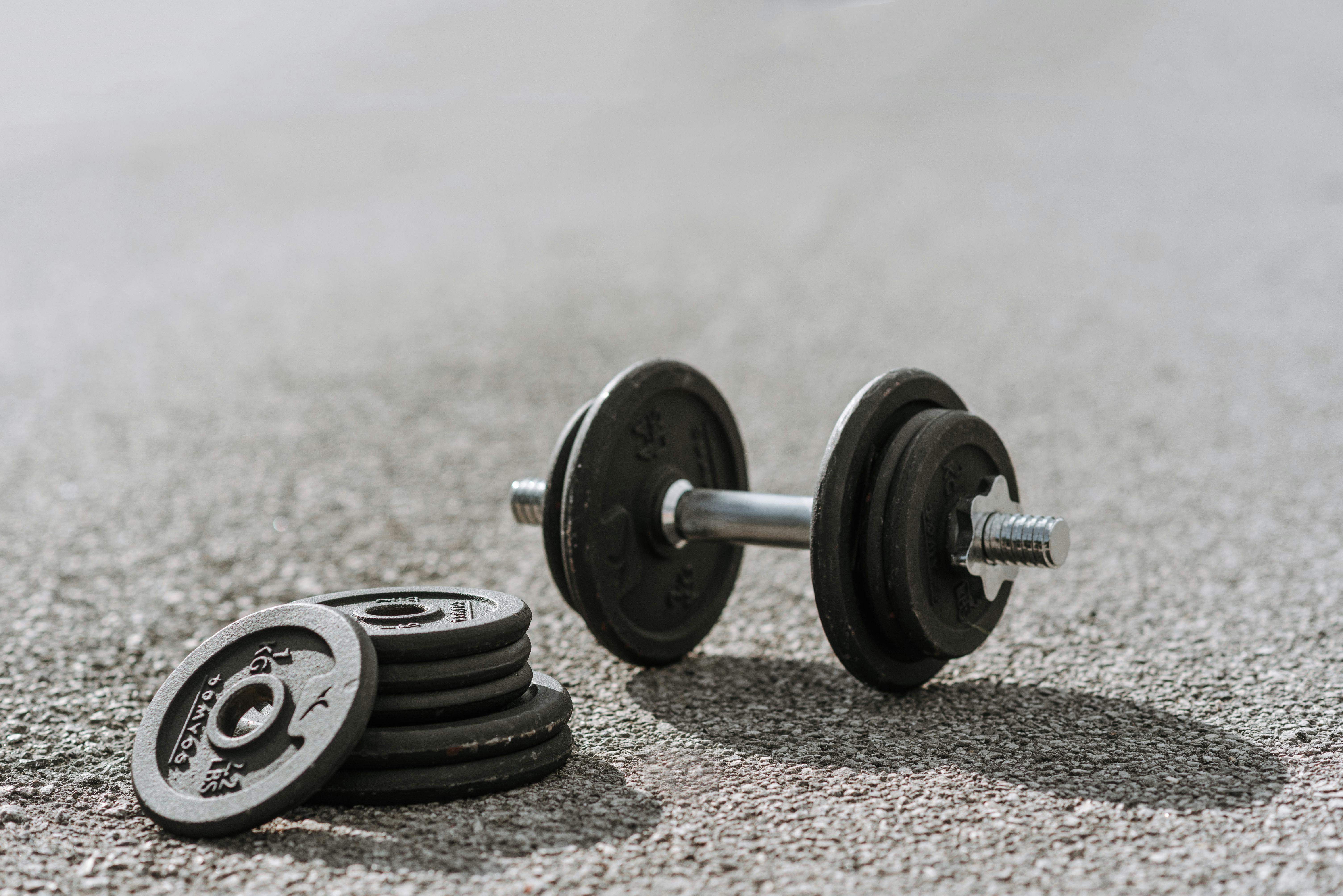 dumbbell near pile of plates on pavement in sunlight