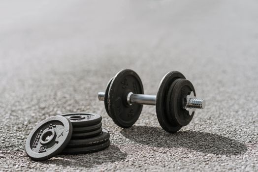 Dumbbell near pile of plates on pavement in sunlight