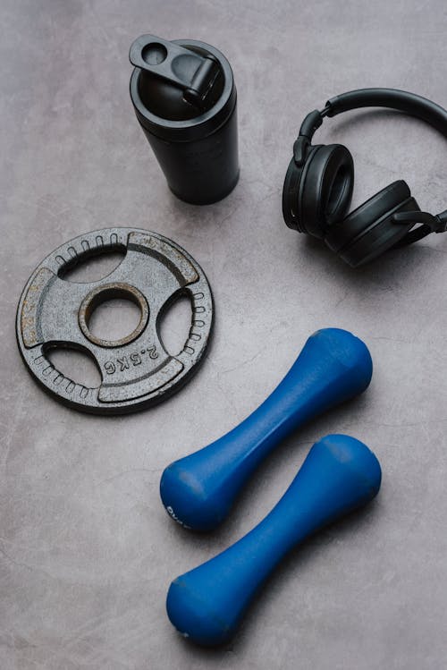 From above of dumbbells with plate and fitness bottle near contemporary wireless headphones on gray background