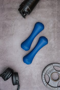 Top view of blue dumbbells, headphones, and gym plate on gray surface.