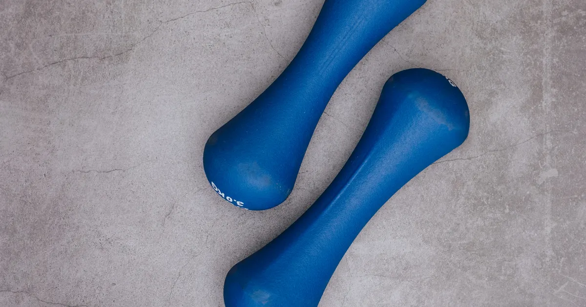 A pair of light dumbbells and a water bottle on a gym floor