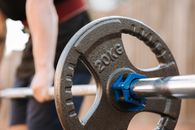 Side view of crop anonymous male athlete preparing to lift barbell with stainless steel bar and plastic collar in daylight