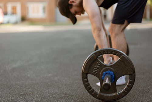 Crop sportsman preparing to lift barbell on pavement