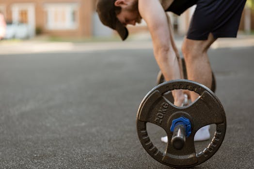 A young male athlete lifting a barbell outdoors on an urban street.