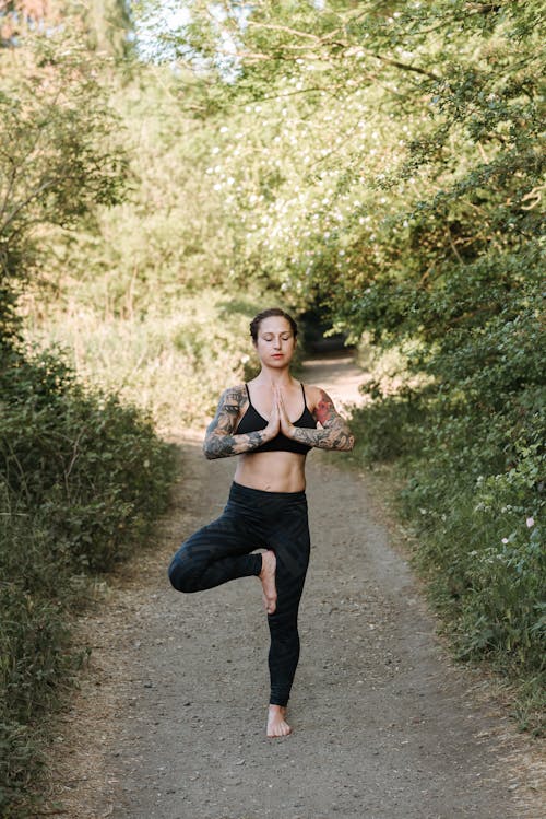 Mindful woman performing Tree pose on walkway between trees