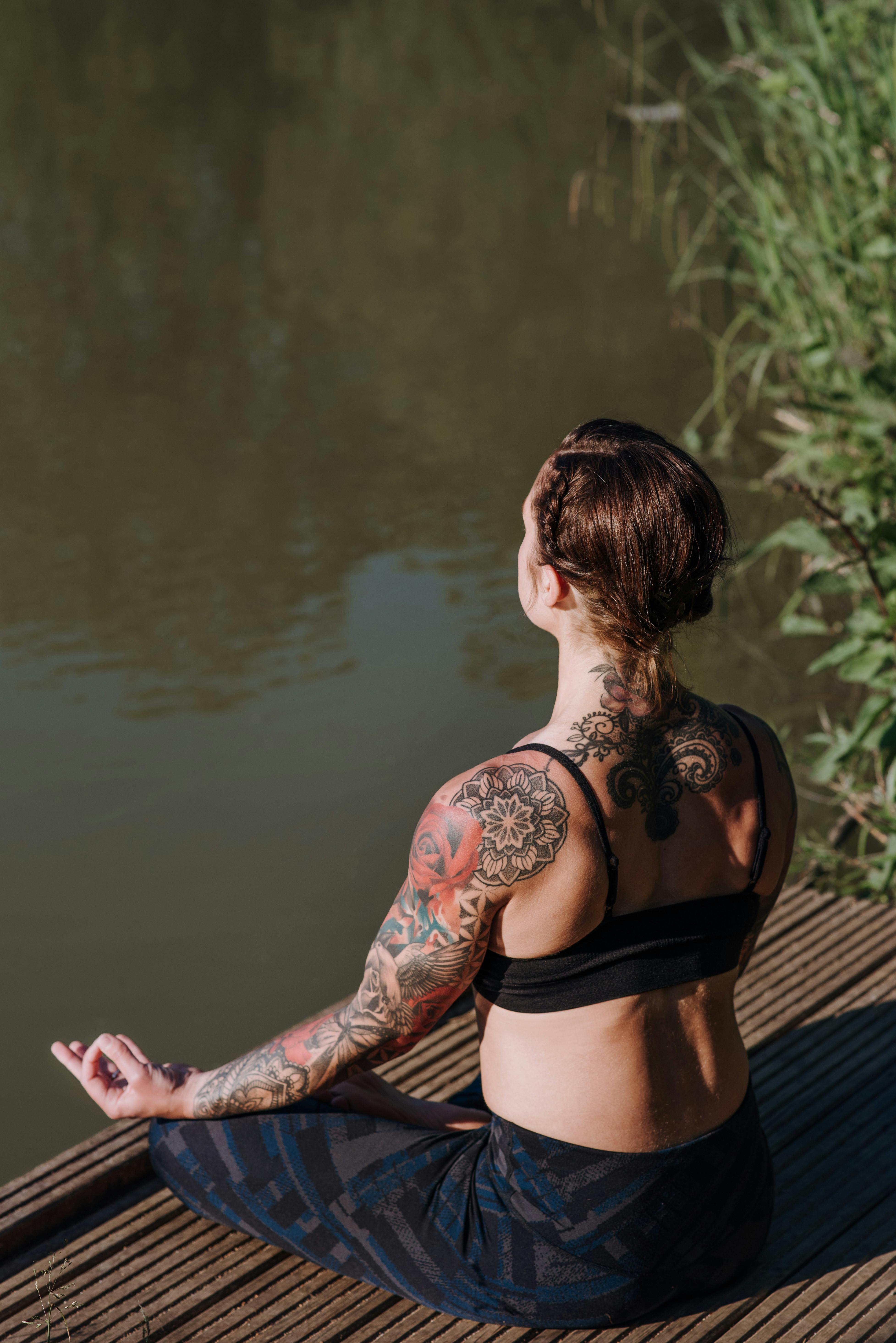 Crop slim tattooed woman with yoga mat against river · Free Stock