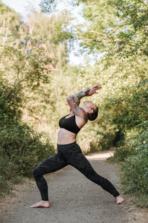 Tattooed woman practicing yoga on pathway between trees