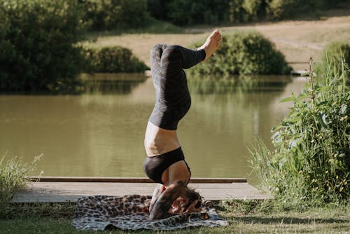 Free Unrecognizable woman standing on head while practicing yoga against pond Stock Photo