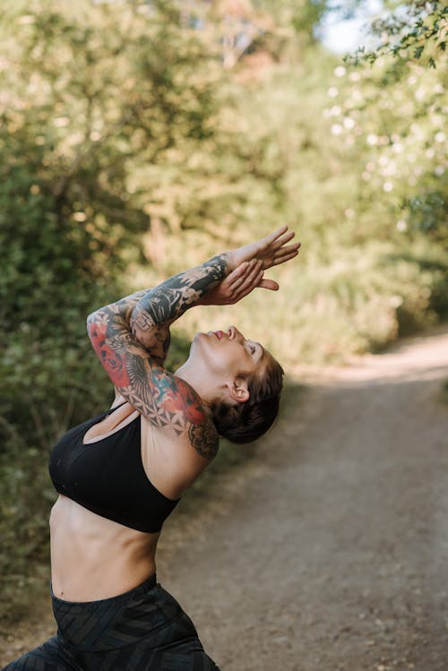 Tattooed woman practicing yoga on walkway in summer