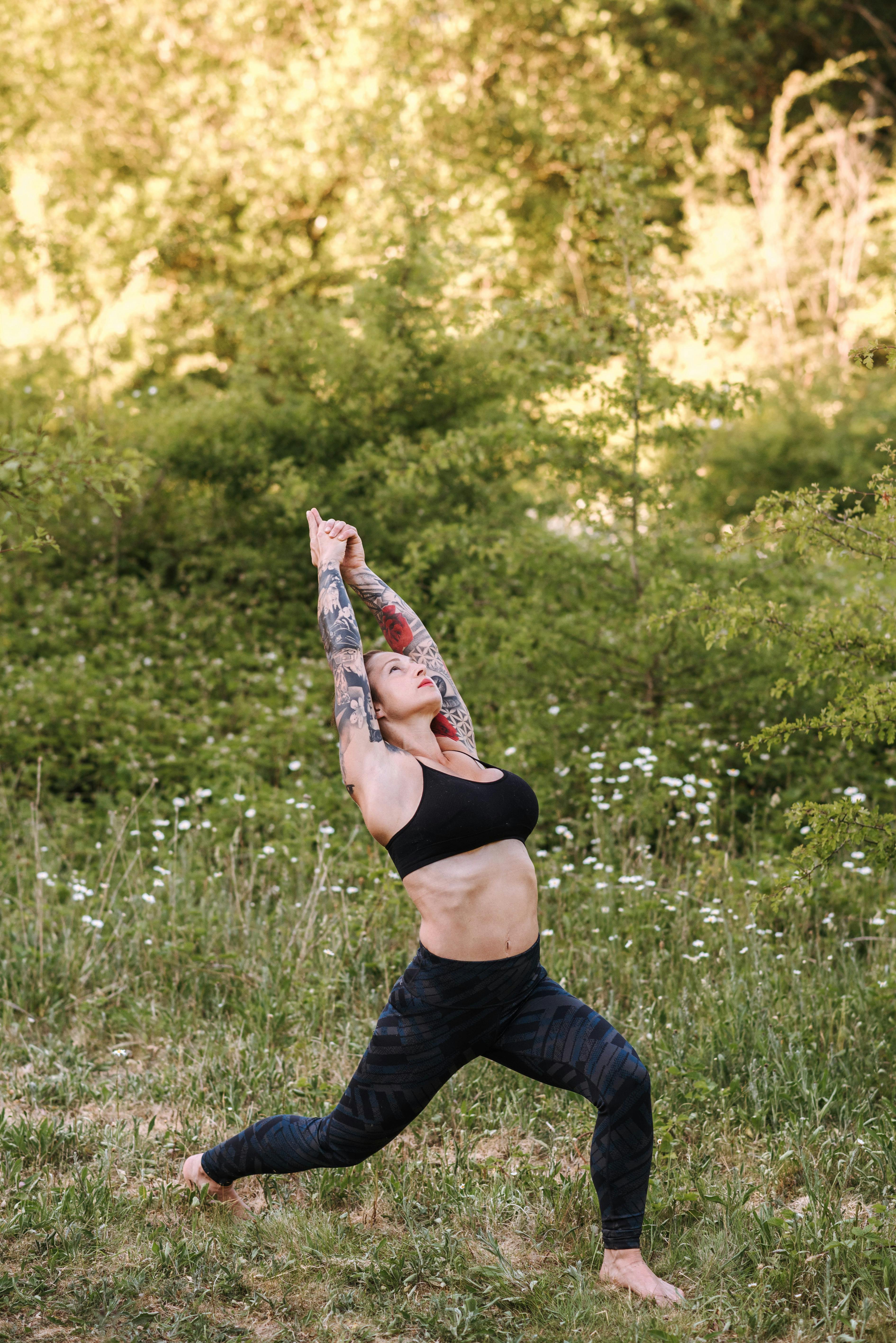 Attentive tattooed woman showing Warrior pose on grass
