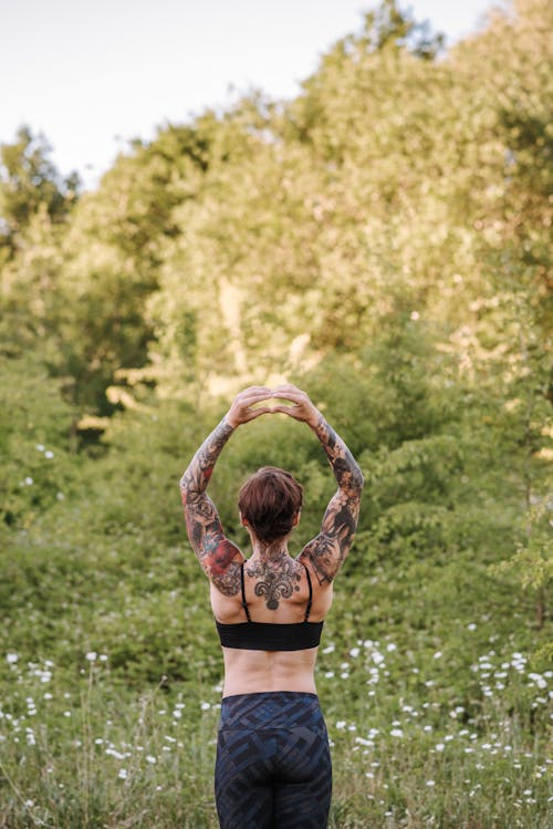 Faceless tattooed woman practicing yoga on meadow