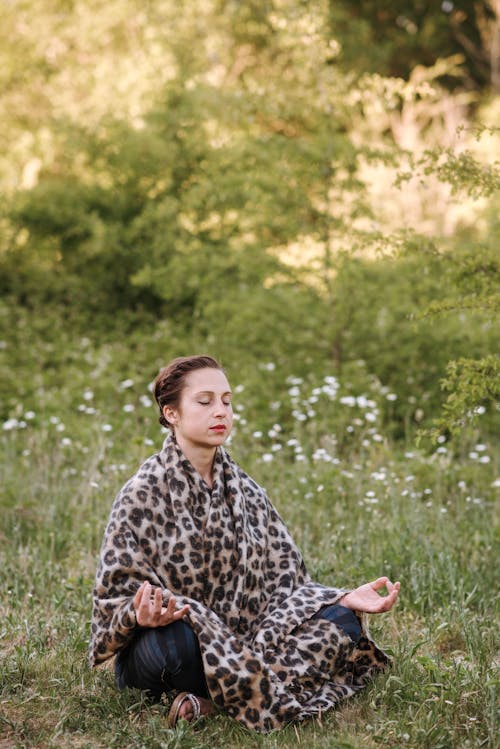 Young concentrated female with closed eyes and plaid sitting with crossed legs while practicing yoga on grass
