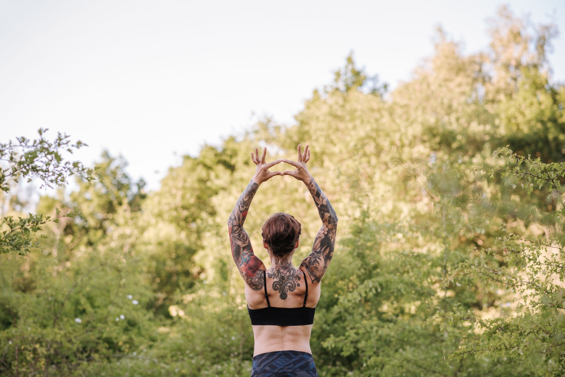 瑜珈如何幫助你度過情緒低潮:簡單技巧緩解壓力 Back view of faceless female in sportswear standing with raised arms while practicing yoga on summer day