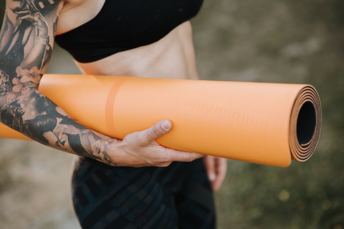 Crop slim tattooed woman with yoga mat against river · Free Stock