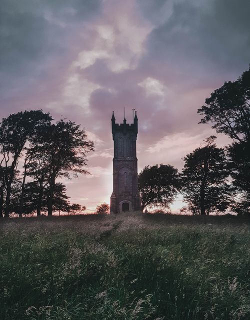 Free A dramatic view of a tower surrounded by trees and fields at twilight in Scotland. Stock Photo