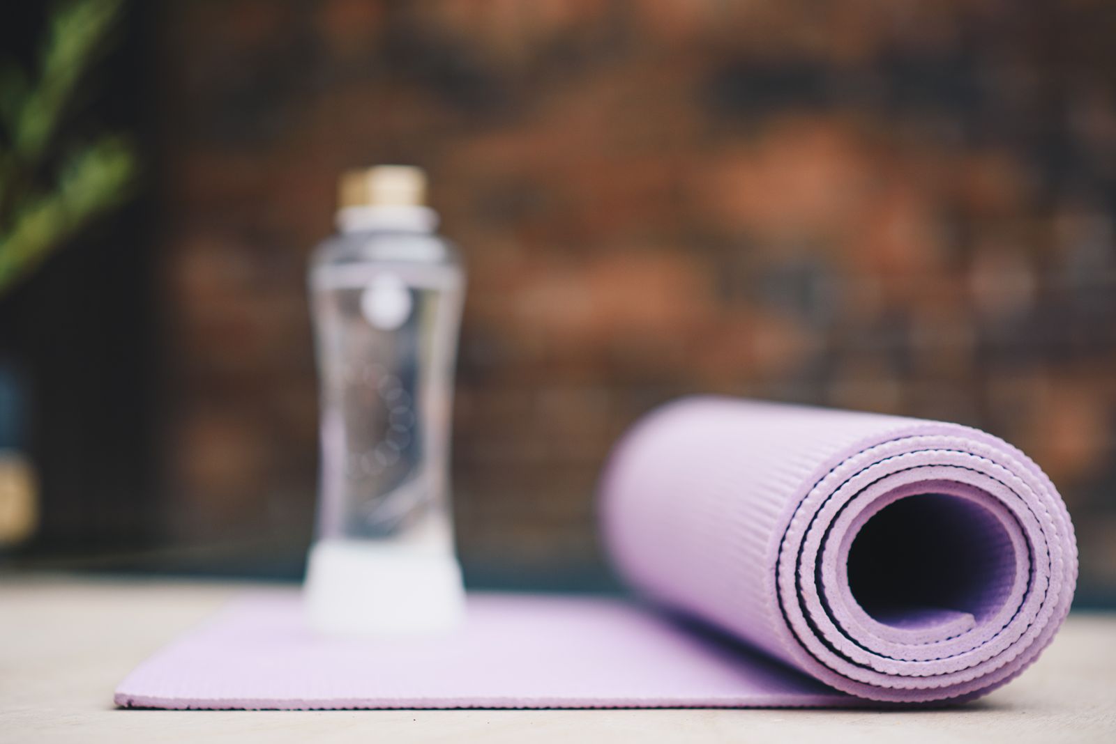 Rolled yoga mat resting next to a bottle of water in warm sunlight, ready for cleaning