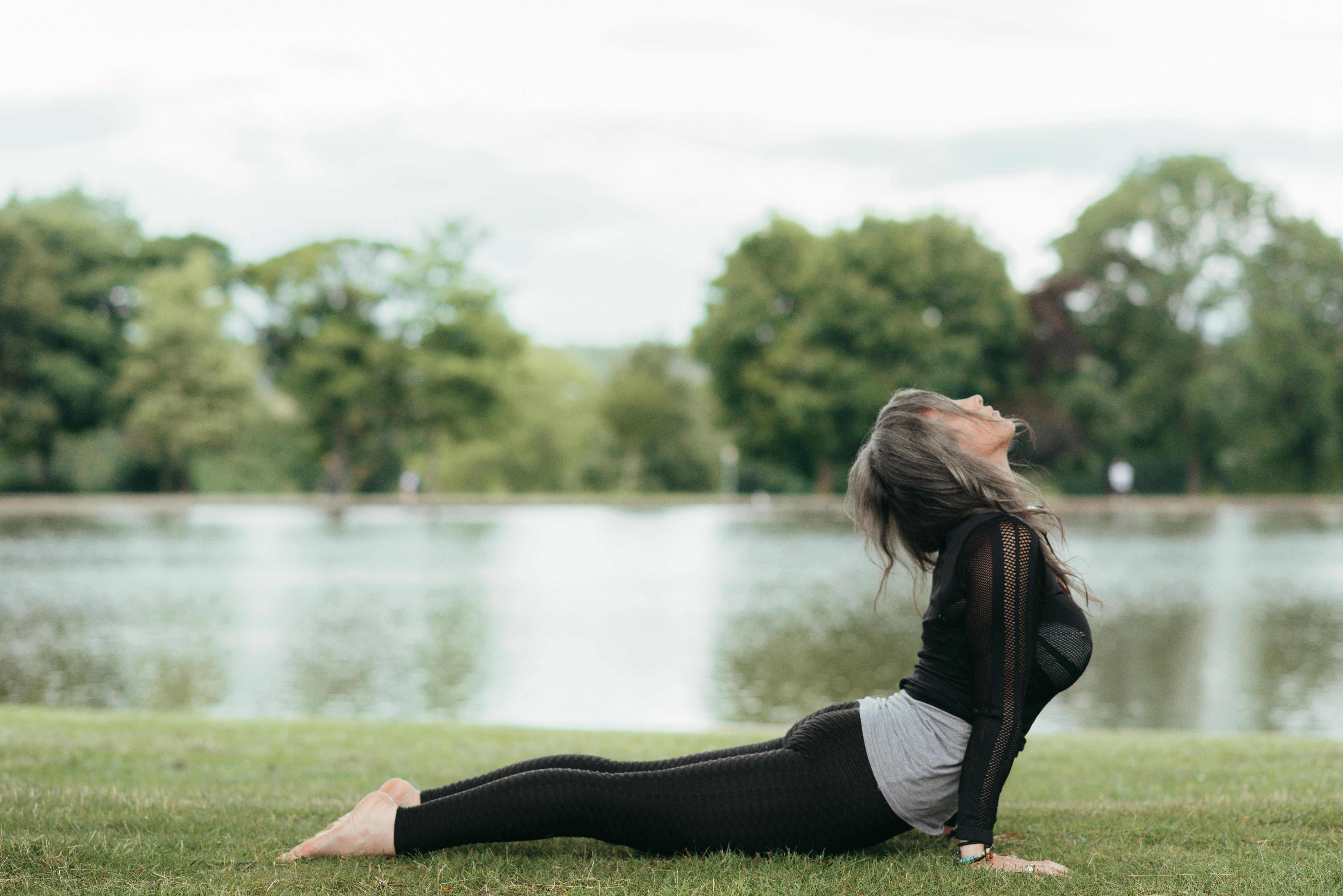 unrecognizable woman practicing yoga against pond in summer