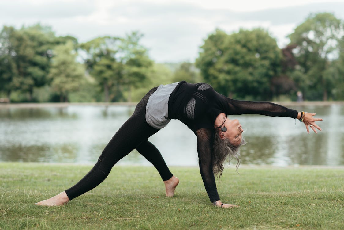 Flexible woman performing Wild Thing pose on grass coast