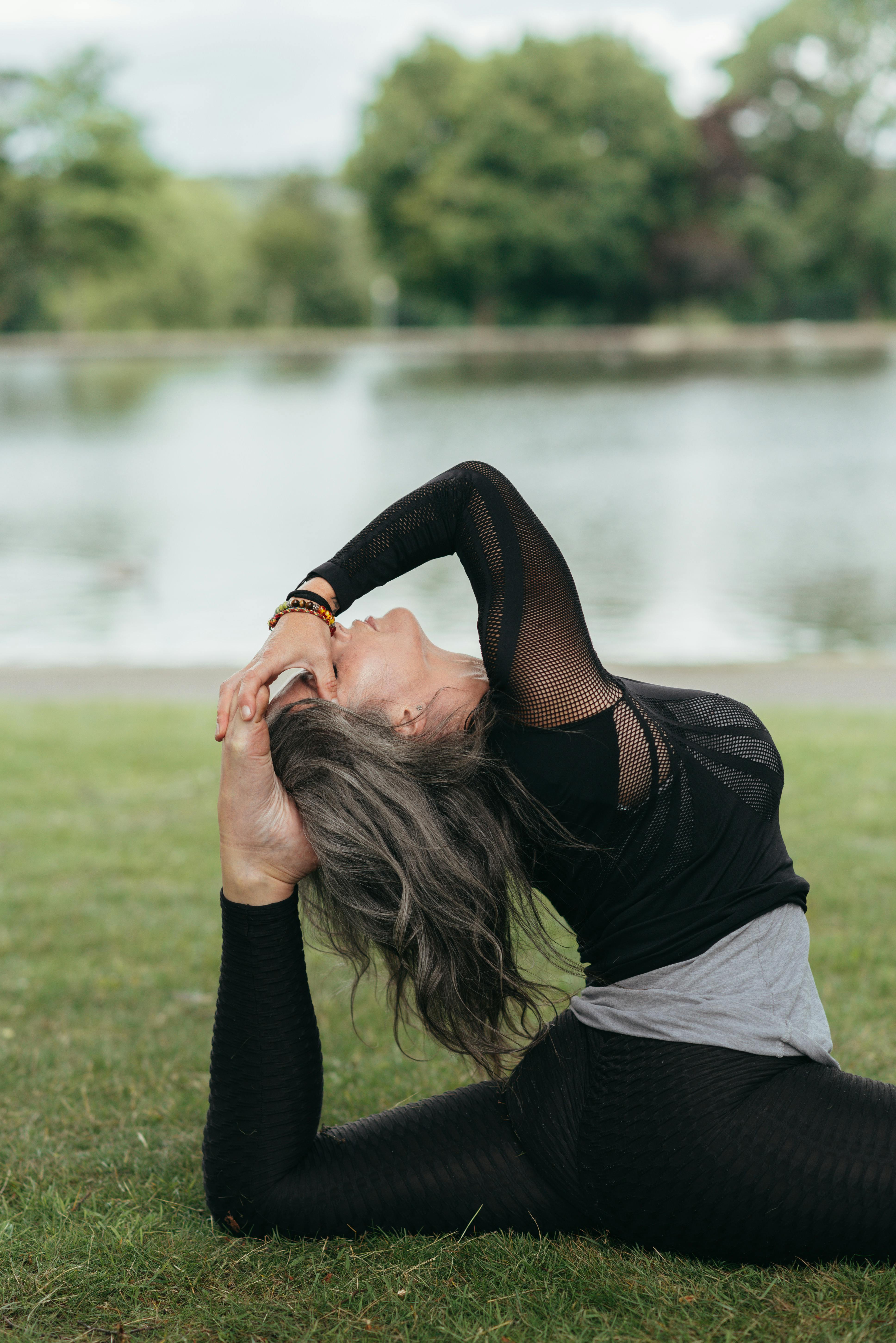Side view of young mindful female sitting in Hanumanasana pose with raised leg and closed eyes while practicing yoga against river