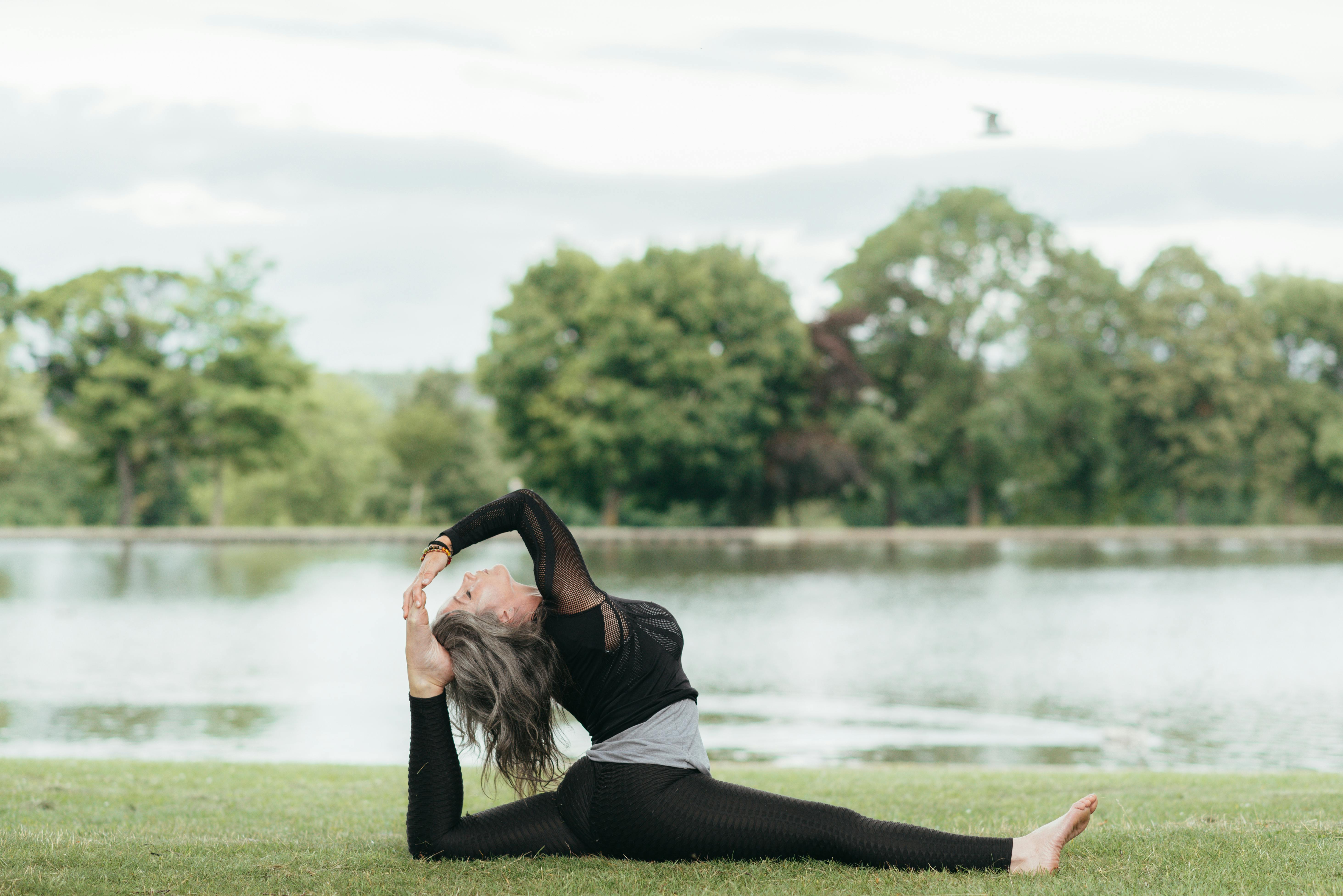 Side view of young flexible female in sports clothes sitting in Front Splits pose with raised leg on grass shore