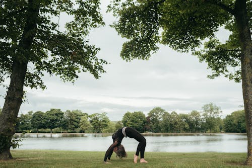 Side view of anonymous slim lady in sportswear standing in Urdhva Dhanurasana pose while practicing yoga on river shore
