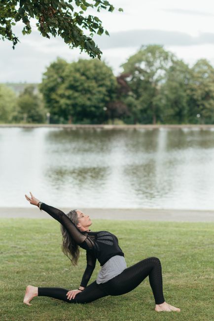 Side view of young barefoot lady in sportswear stretching legs while practicing yoga with raised arm against river
