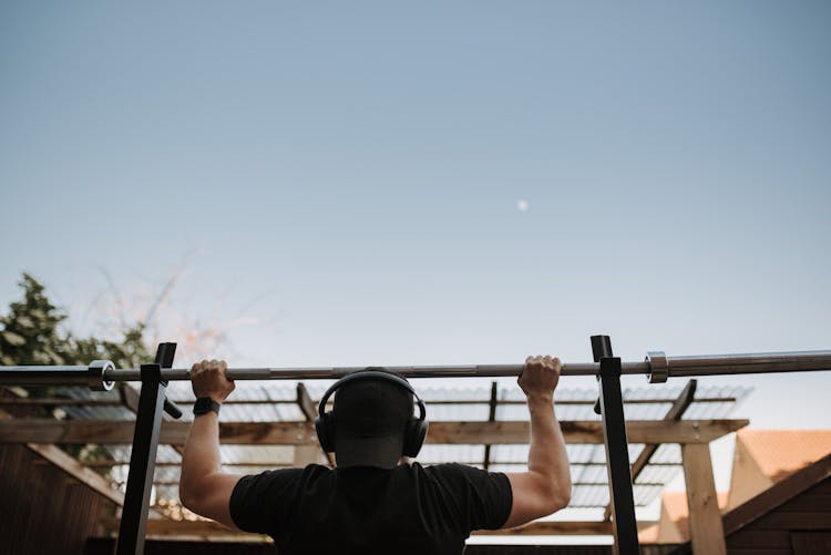 Unrecognizable Sportsman In Headset Pulling Up On Bar On Street