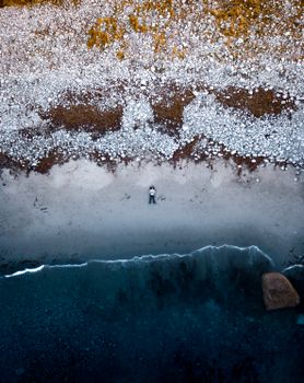 Drone shot capturing a person lying on a peaceful rocky beach by the sea.