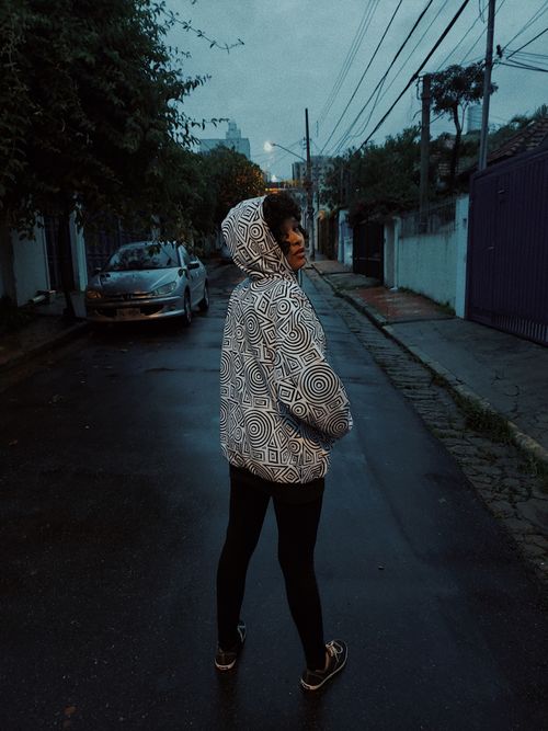 Free A young woman in a patterned hoodie stands on a São Paulo street at twilight, exuding style and mystery. Stock Photo