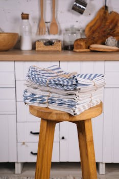 Neatly stacked blue and white kitchen towels on a wooden stool in a cozy kitchen setting.