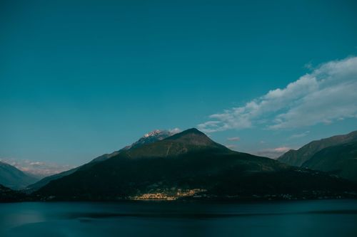 Free Scenic view of majestic volcanic hills with small village located near calm vast lake under clear blue sky Stock Photo
