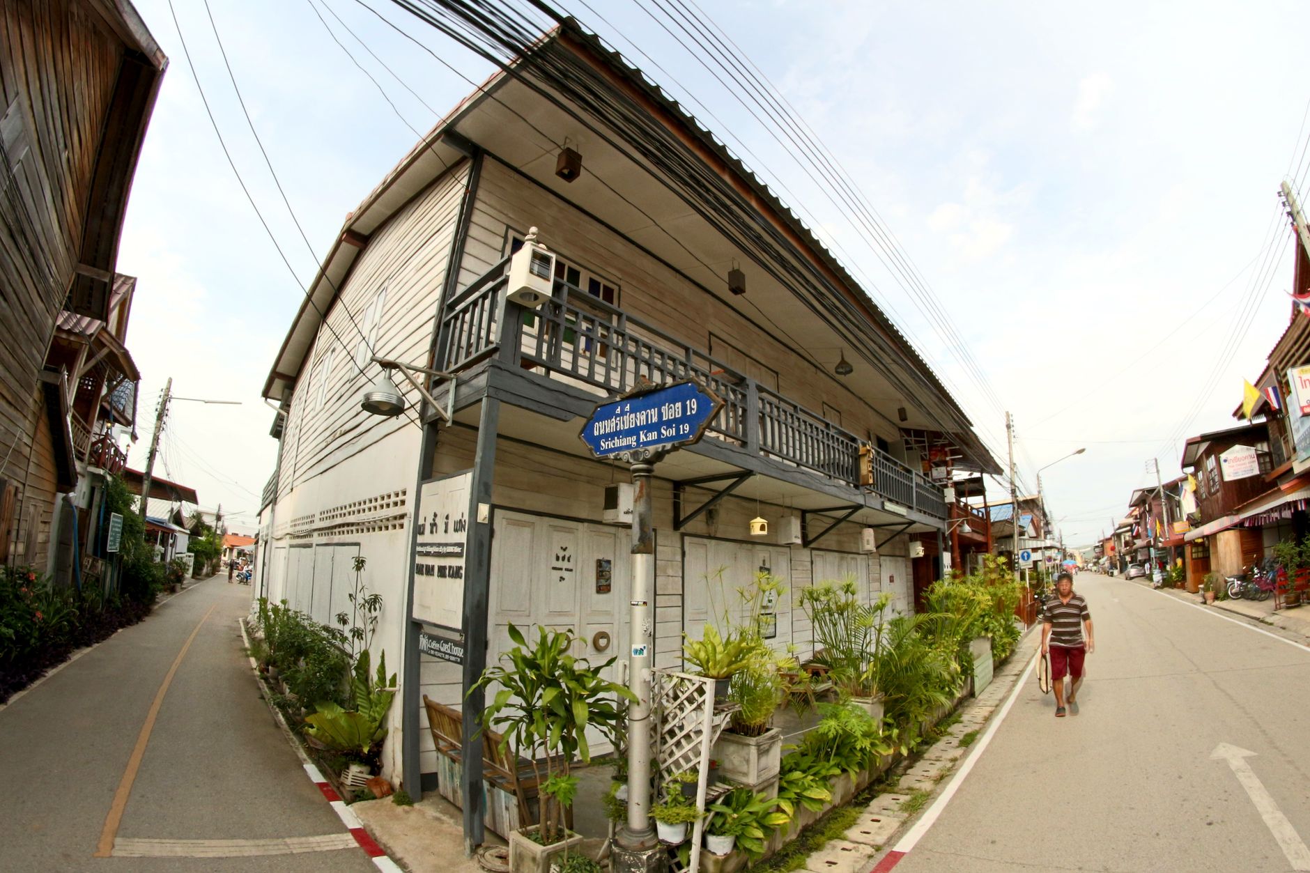 A rural Thai roadside viewed from a safe distance, parked motorcycles near a fenced compound at dusk