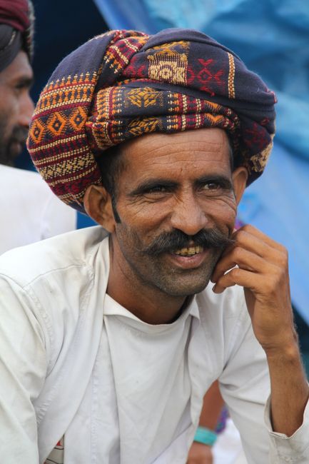 Smiling elderly man in a colorful turban with a relaxed pose outdoors.
