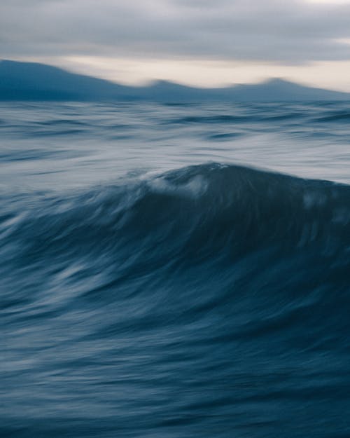 Scenery view of sea with high fast water flow behind mount silhouettes under cloudy sky in twilight