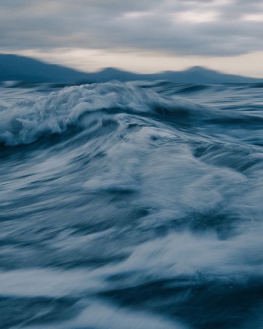 Scenic view of ocean with rapid splashing water flow behind mountain silhouettes under cloudy sky in evening