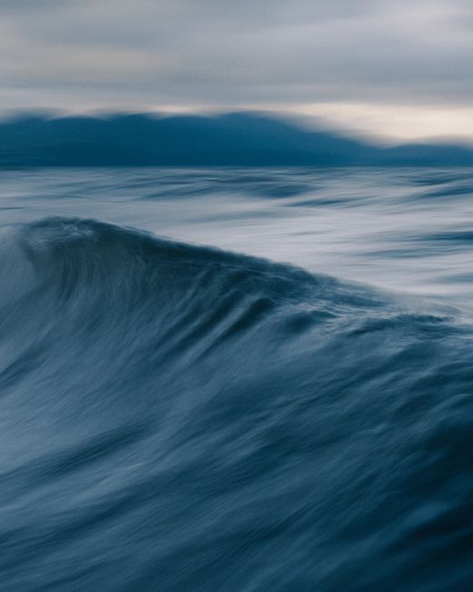 Spectacular view of stormy ocean with fast water fluid behind mountain silhouettes under cloudy sky at sundown