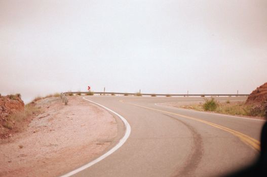 在灰色天空下，沥青铺就的弯曲道路穿过风景优美的乡村，路面上清晰可见道路标记