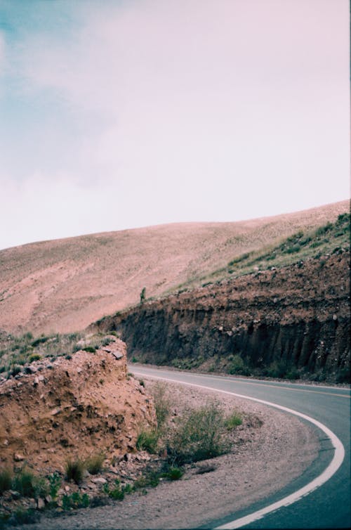 Free A peaceful curved road traverses through dry rolling hills under a cloudy sky. Stock Photo