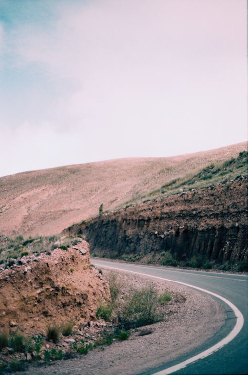 Free A peaceful curved road traverses through dry rolling hills under a cloudy sky. Stock Photo
