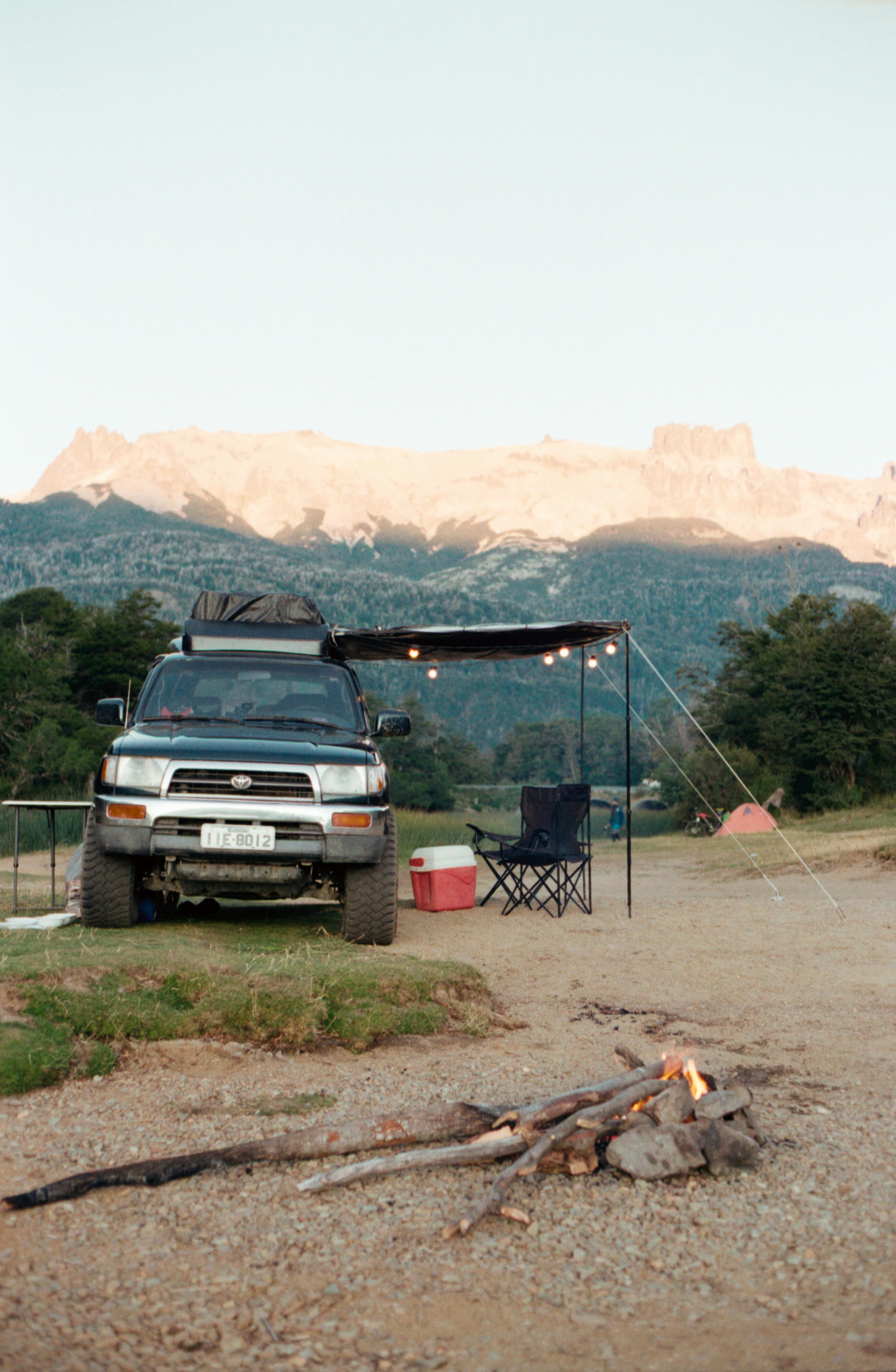 A tranquil mountain campsite scene with a truck, bonfire, and tent during the day.