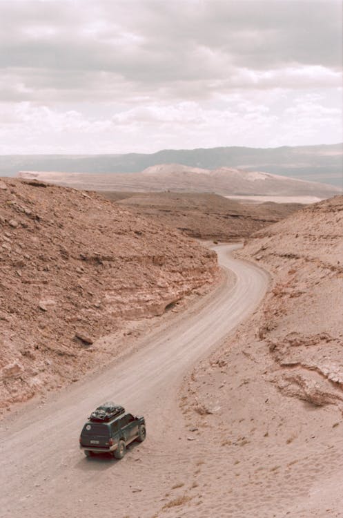 Black Vehicle on Dirt Road Between Hills