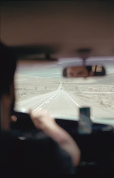 Blurry view through car windshield of a man driving down a long open road, with focus on the landscape ahead.