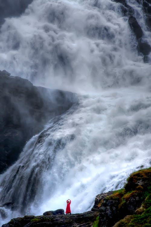 Person Standing on the Cliff Beside a Water Falls 