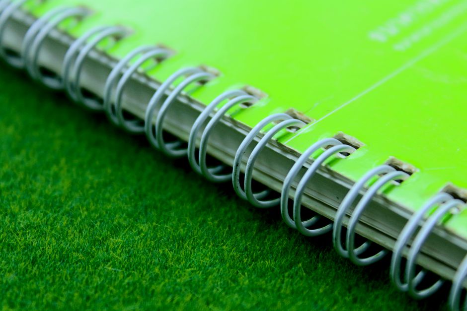 Green spiral notebook on grass, close-up detail with copy space.