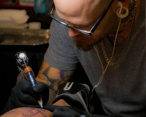Free Close-up of a skilled tattoo artist using a machine to ink a client's arm in a studio setting. Stock Photo