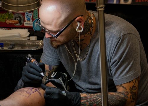 Free Tattoo artist working intently with a machine, highlighting body art creation process. Stock Photo