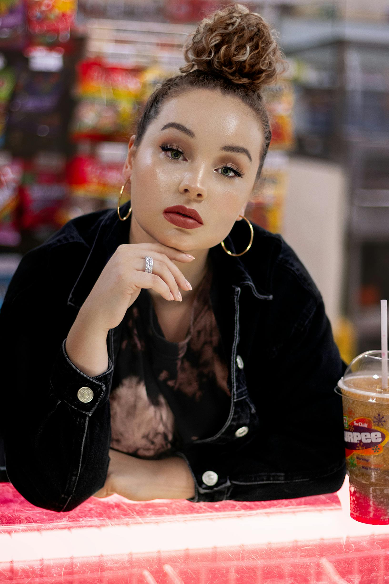 A woman posing confidently in casual wear, with hoop earrings and a soft drink indoors.